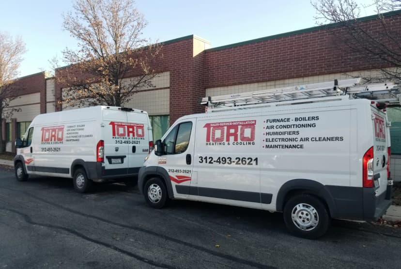 Two TORO Heating & Cooling service vans parked outside a brick building.