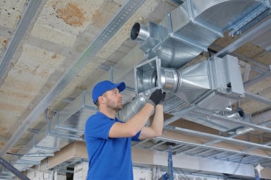 Worker installing HVAC ductwork in a ceiling