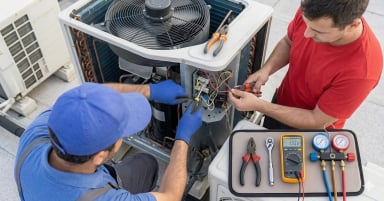 Two technicians repairing an air conditioning unit on a rooftop.